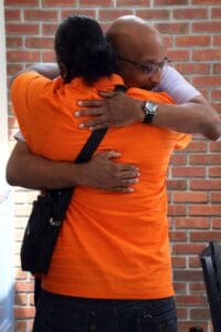 A man and woman hugging in front of a brick wall.