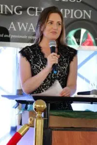 A woman is speaking at an event with microphone.