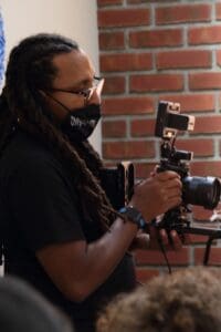 A man with dreadlocks holding a camera.