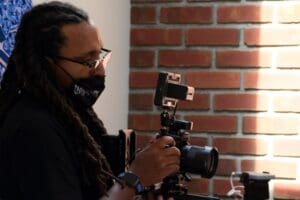 A man with dreadlocks holding a camera.