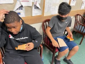 Two boys sitting on chairs eating a sandwich.