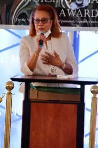 A woman is speaking at an event with her hands raised.