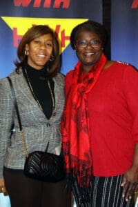 Two women standing next to each other in front of a blue wall.